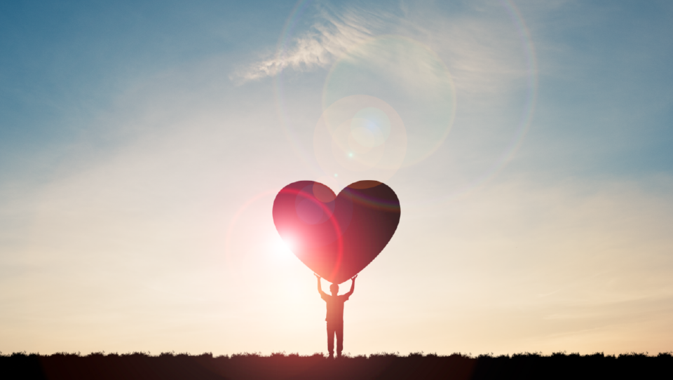 Someone holding a heart during a sunrise