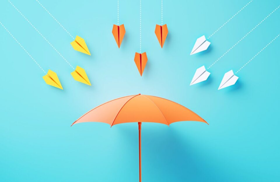 Colorful paper airplanes fly at an orange umbrella